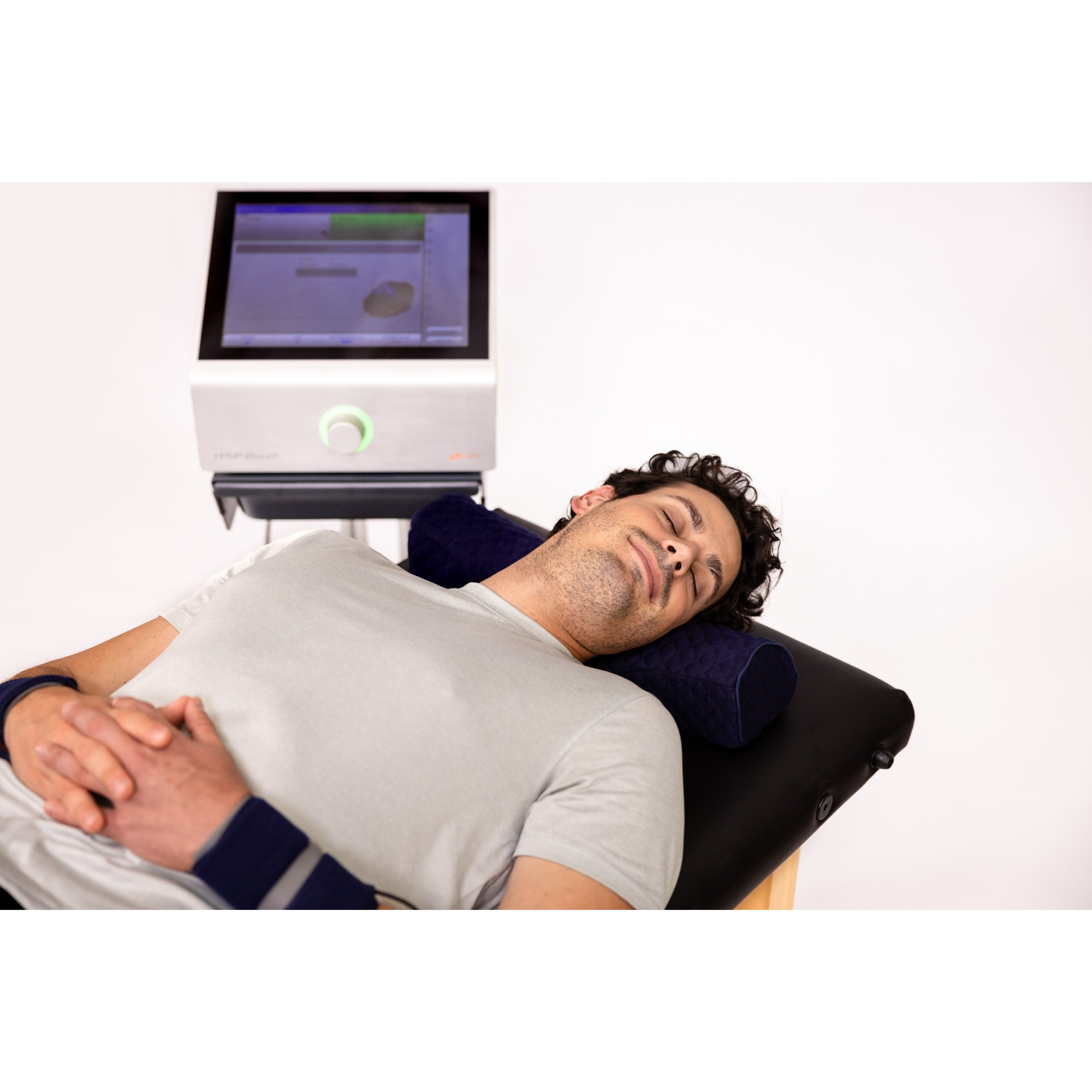 Manufacturer treatment illustration: A relaxed man receiving HiToP treatment with wrist electrodes beside the device.