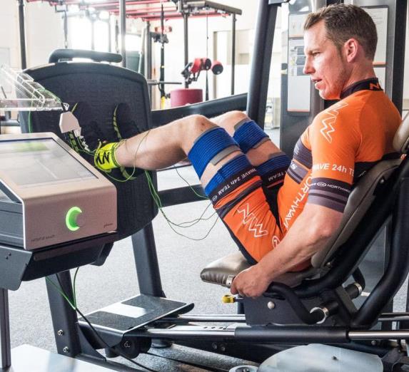 Manufacturer photograph of a man in orange performing a leg press with HiToP thigh electrodes and equipment